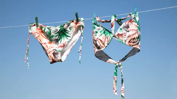 A tropical print bikini hanging on a clothesline against a clear blue sky