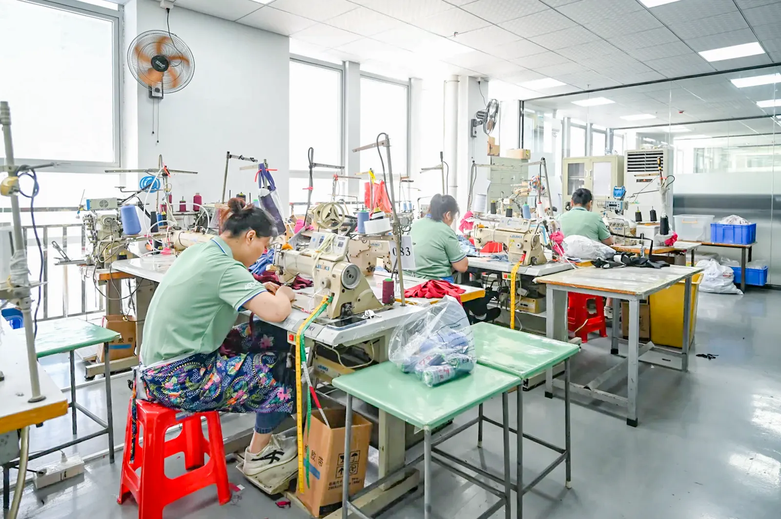 Sample room at ASG Fashions with sewers working at sewing machines beside fabric bags and worktables