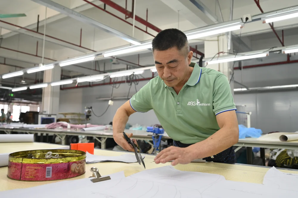 Pattern maker in an ASG uniform cutting a paper pattern by hand with large scissors