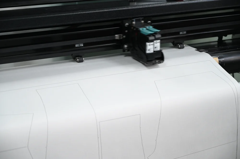 Pattern plotter drawing garment pattern lines on white pattern paper
