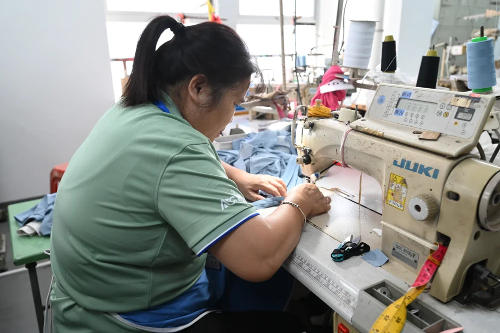 Sewer stitching blue fabric on a lockstitch machine at her workstation