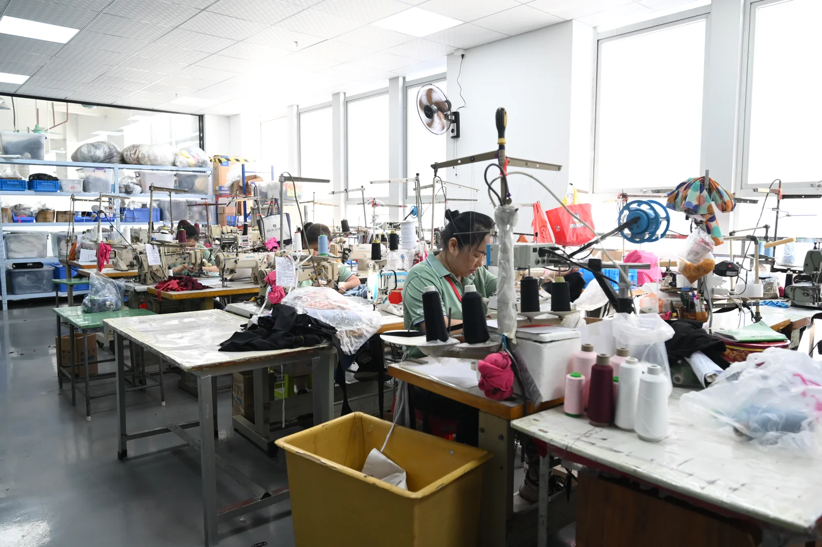 Sample room with rows of sewing workstations, fabric bags and worktables